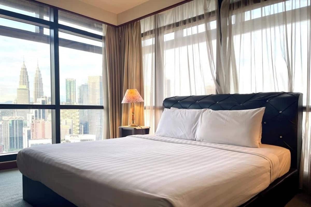 A hotel room with a large bed, a nightstand with a lamp, and a view of the city skyline.