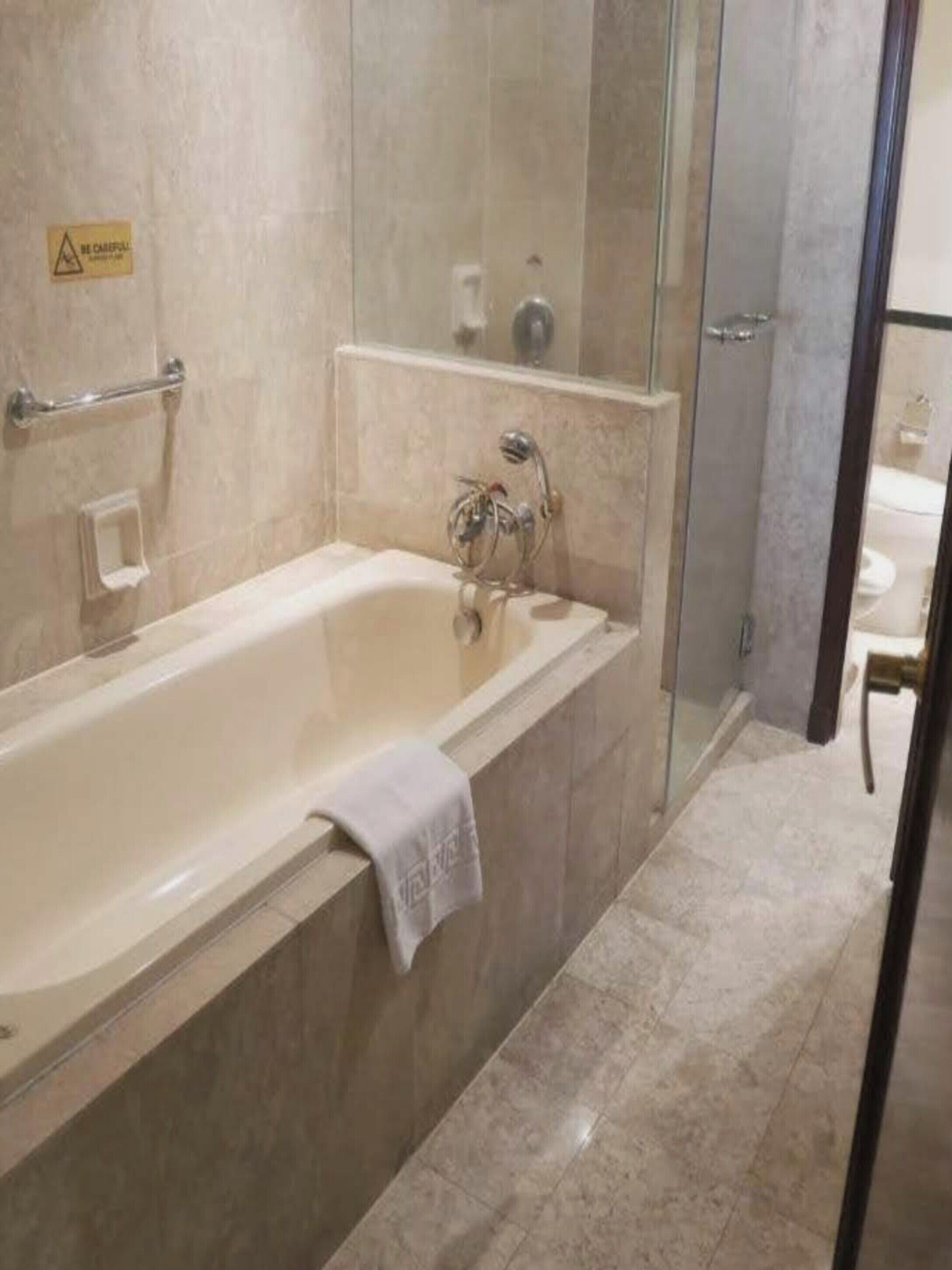 A bathroom with a bathtub, a glass shower enclosure, and a toilet visible through the glass.