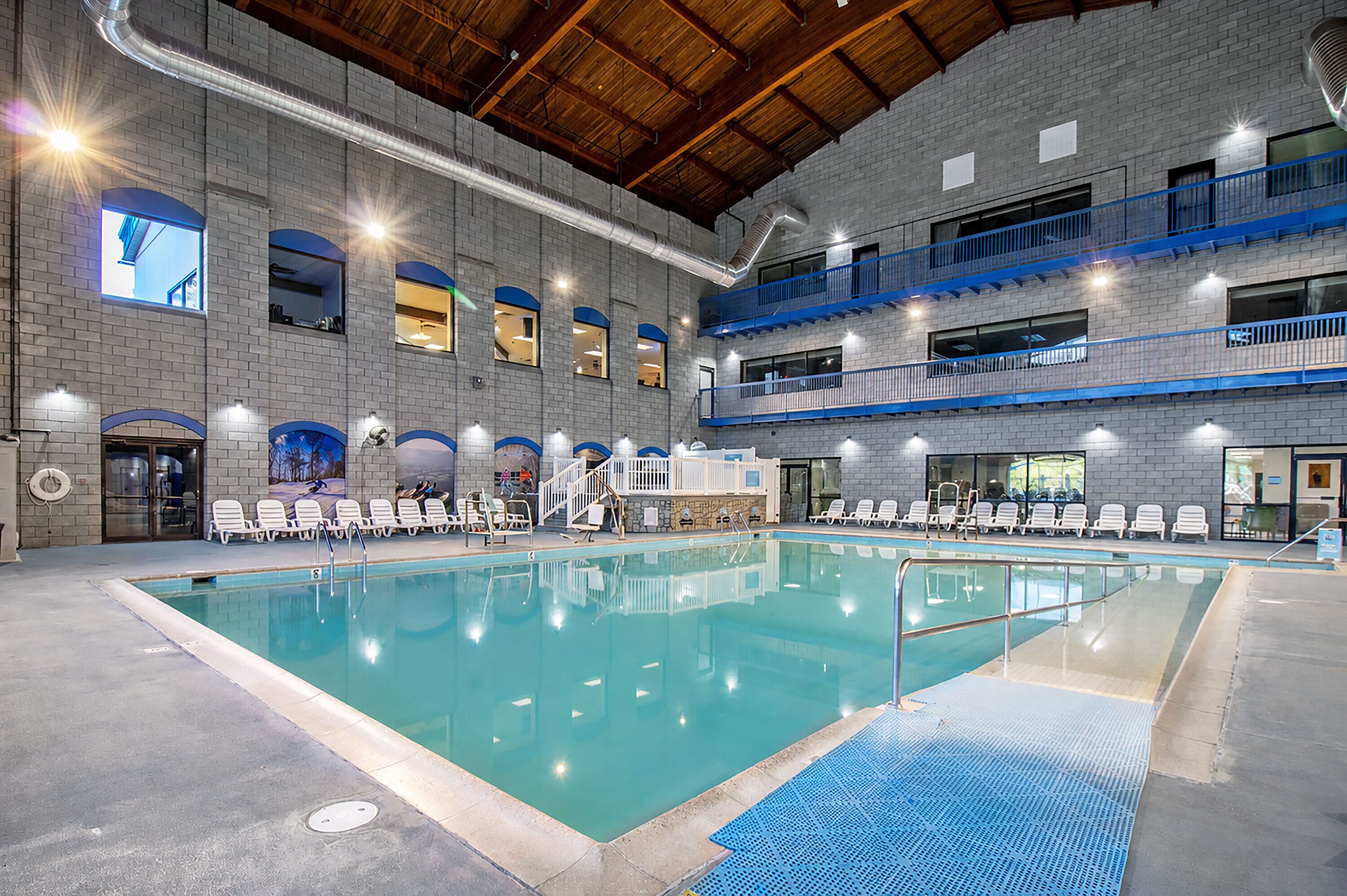 An indoor swimming pool with multiple levels of balconies, a brick wall, and a clear pool area.
