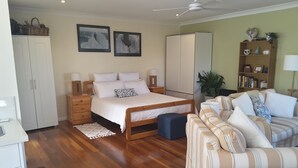 A bedroom with a bed, bedside tables, a wardrobe, a sofa, and a bookshelf. - Cosy Bayside Studio - Spring Into Relaxation By The Bay (Manly West)