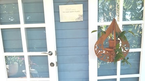 A wooden door with frosted glass panels, a welcome sign, a potted plant, and a white pedestal with a flower. - Cosy Bayside Studio - Spring Into Relaxation By The Bay (Manly West)