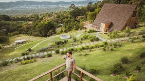 A wooden deck with a table and chairs, overlooking a landscaped garden and a hilly landscape.
