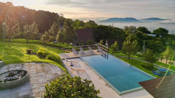 A swimming pool with lounge chairs, surrounded by greenery and a view of distant mountains.