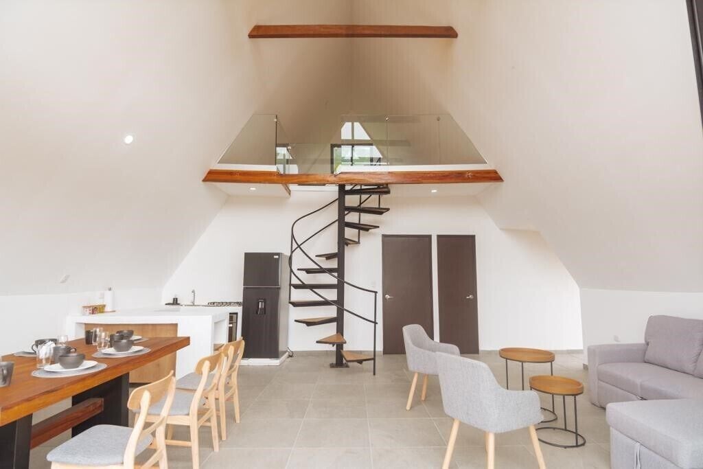 A modern interior with a dining area, a spiral staircase, and a loft space.