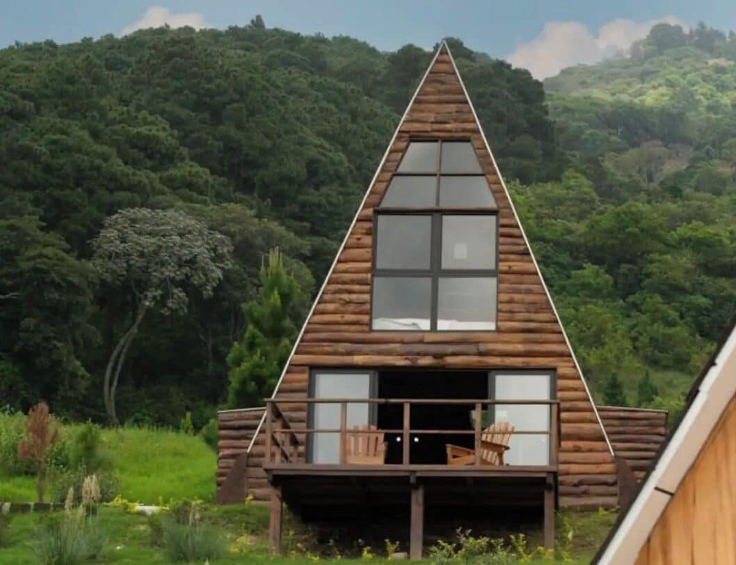 A wooden cabin with a triangular roof, large windows, and a balcony with chairs.