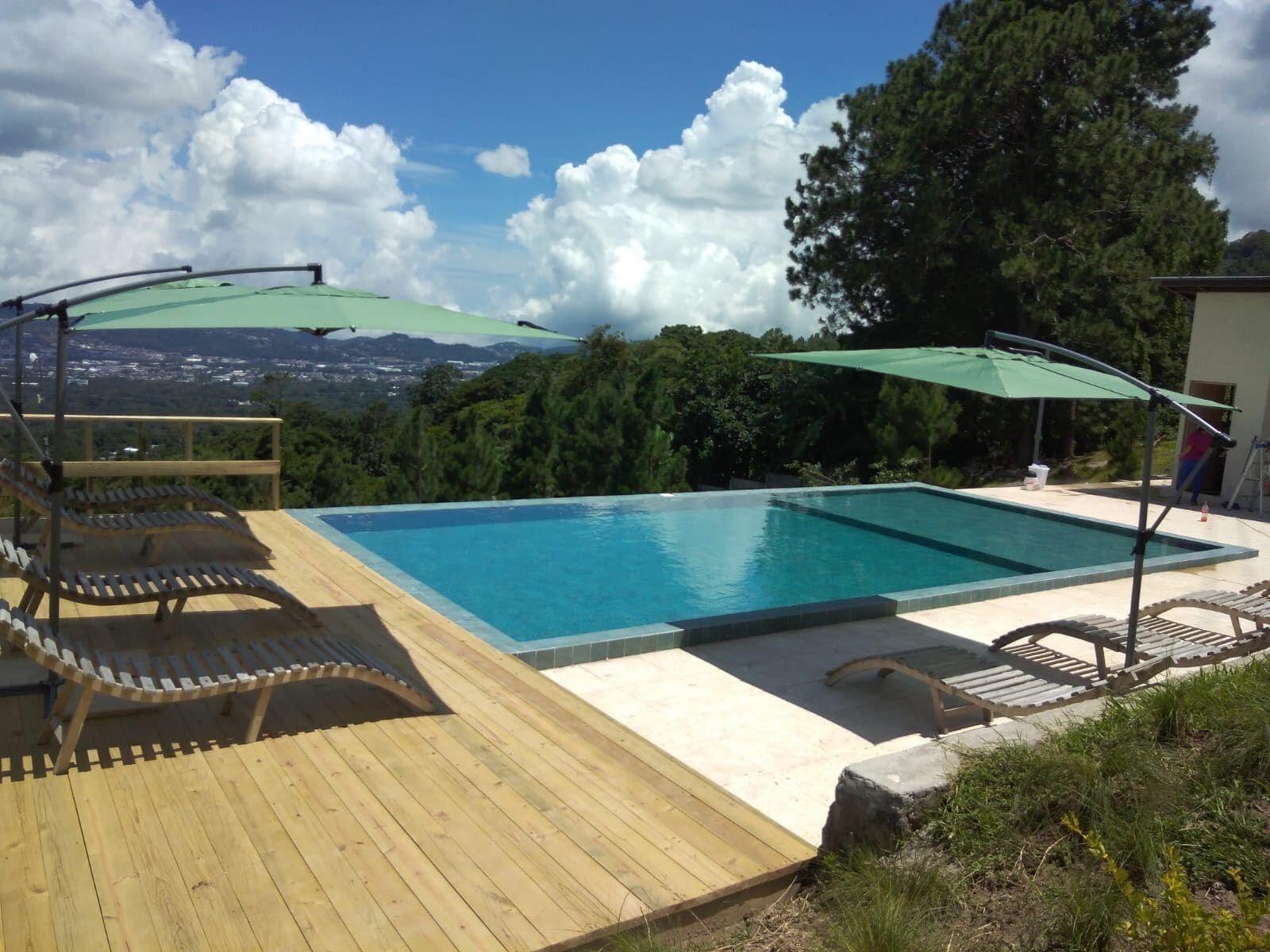 A rectangular swimming pool with a wooden deck and two green umbrellas.