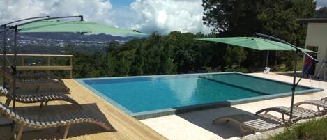 A rectangular swimming pool with a wooden deck and two green umbrellas.