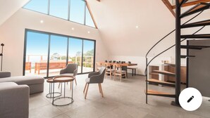 A spacious loft with a high ceiling, large windows, a dining area, and a spiral staircase.