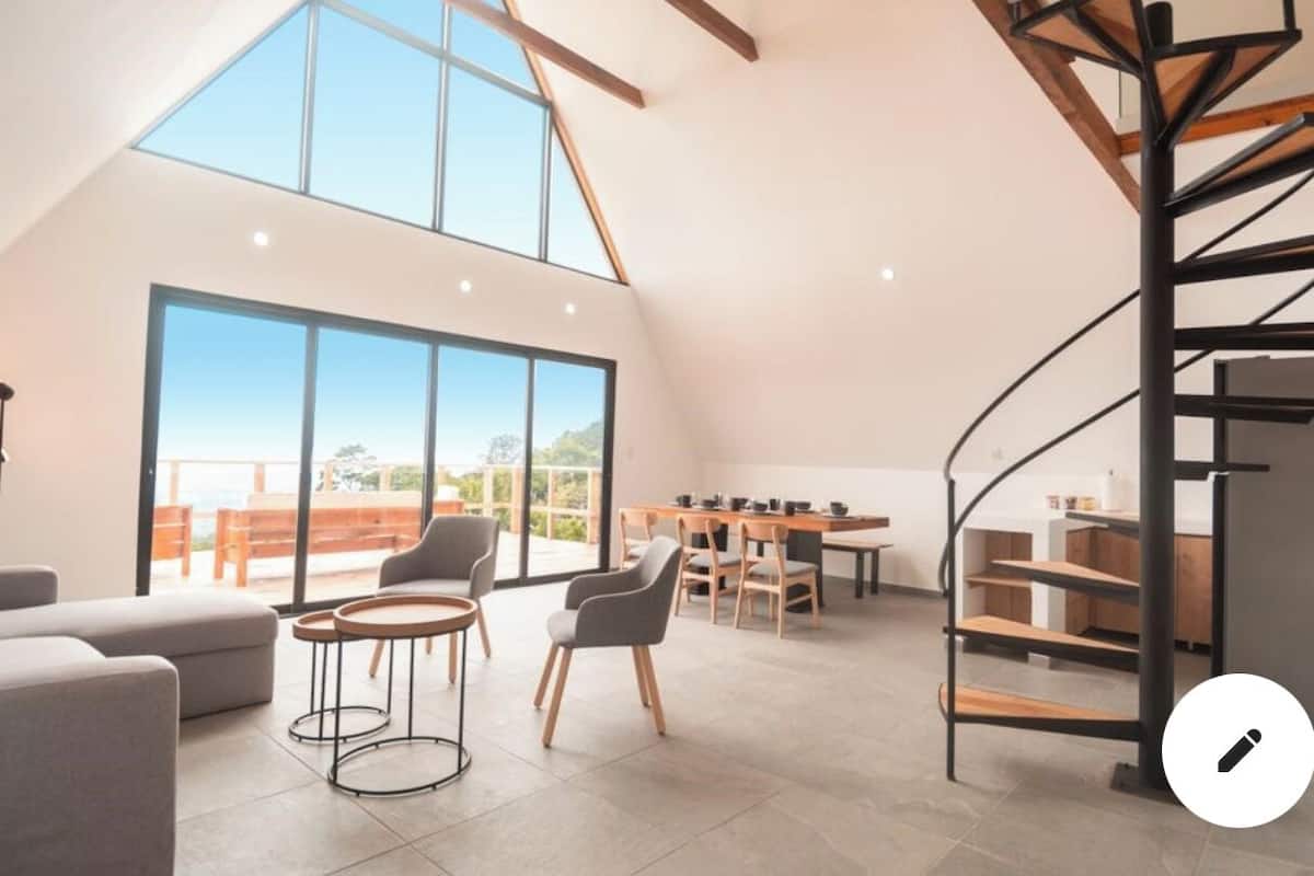 A spacious loft with a high ceiling, large windows, a dining area, and a spiral staircase.