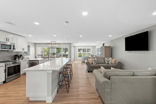A modern kitchen with white cabinets, a central island with stools, a built-in oven, and a microwave.