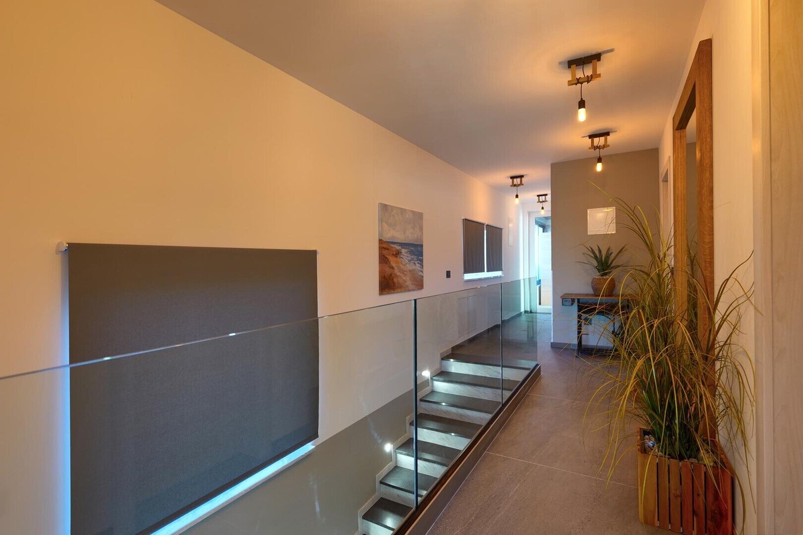 A modern hallway with a glass railing, a staircase, and a wooden bench with plants.