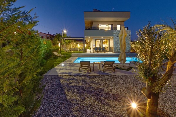 Una casa moderna a due piani con piscina, area salotto esterna e patio ben illuminato.