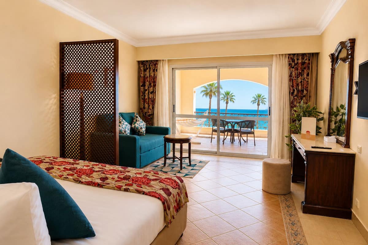 Habitación de hotel con cama, escritorio, silla, una mesita y vista a la playa.
