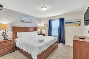 A neatly made bed with white linens, a wooden headboard, and a bedside table with a lamp. - Family-Friendly Villa w Pool, Hot Tub & Game Room (Kissimmee)