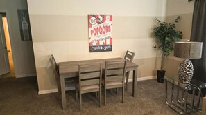A dining area with a wooden table and chairs, a wall-mounted poster, a potted plant, and a lamp. - Family-Friendly Villa w Pool, Hot Tub & Game Room (Kissimmee)
