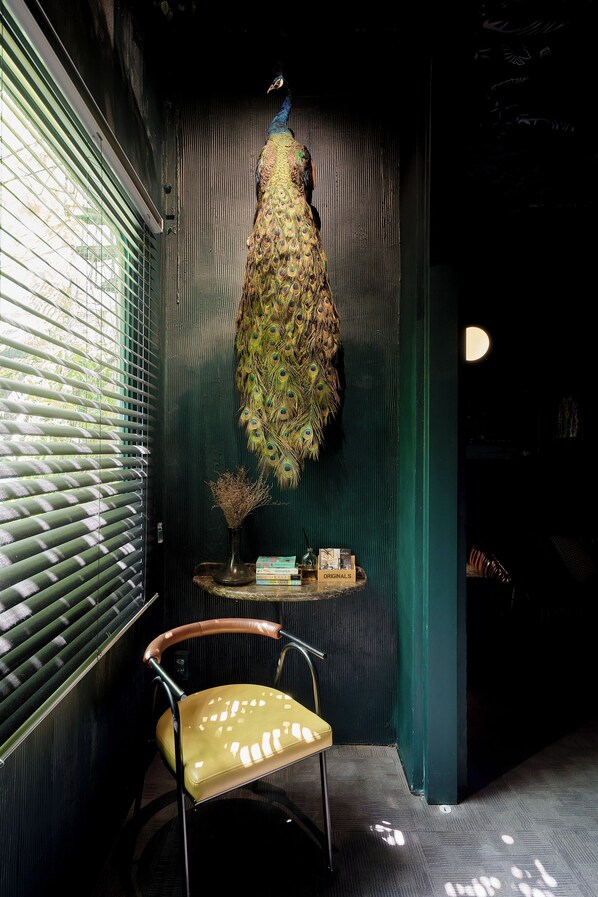 Una habitación con una decoración de pluma de pavo real, una silla y una mesita con libros y un jarrón.