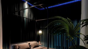 Quarto moderno com cama, luminárias de cabeceira e uma grande planta em vaso.
