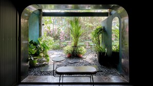 Um pequeno espaço de pátio murado, com um banco, plantas em vasos e vista para um jardim.