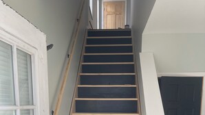 A staircase with alternating dark and light wooden steps, white walls, and a closed door at the top. - Charming 2-bedroom apartment in delightful Geneva,walking distance to downtown.  (Geneva)