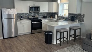 A modern kitchen with white cabinets, a stainless steel refrigerator, a microwave, and a gas stove. There is a small island with stools and a trash can. - Charming 2-bedroom apartment in delightful Geneva,walking distance to downtown.  (Geneva)
