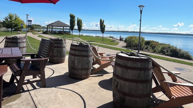 An outdoor seating area with wooden barrels, a red umbrella, and a view of a lake. - Charming 2-bedroom apartment in delightful Geneva,walking distance to downtown.  (Geneva)