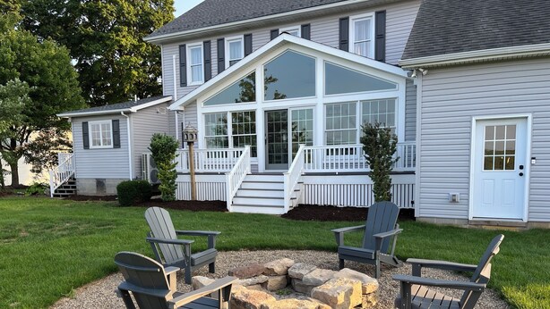 Una casa con una amplia terraza, un brasero y cuatro sillas tipo Adirondack.