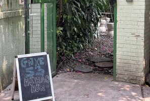 A chalkboard sign with handwritten text, a green door, and a garden area with plants and stepping stones. - Unique Art Decór Studio Hidden inside Coffee Shop (Quan 1)