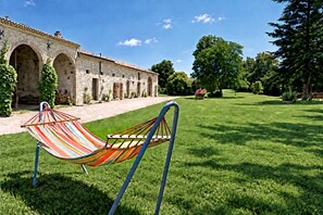 A hammock in a grassy area with a stone building in the background. - Soleil de Cocagne – Old Stone & Charm near the Canal du Midi (Lagarde)