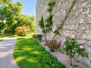 A pathway leading to a building with a stone wall and a garden with roses. - Soleil de Cocagne – Old Stone & Charm near the Canal du Midi (Lagarde)