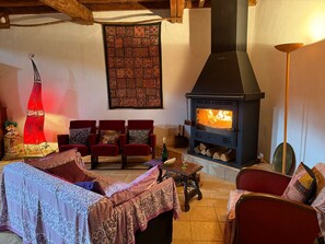A cozy living room with a fireplace, red upholstered chairs, a patterned wall hanging, and a decorative sail.