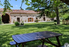 A stone building with a tiled roof, a wooden door, and a picnic table in the foreground. - Soleil de Cocagne – Old Stone & Charm near the Canal du Midi (Lagarde)