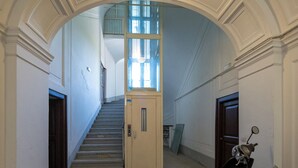 A hallway with a staircase, a door, and a scooter parked to the side. -  De Vivo Realty - La Mela Apartment (Meta)