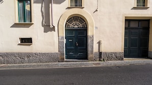 A building with a central arched entrance, two windows on either side, and a number '23' above the door. -  De Vivo Realty - La Mela Apartment (Meta)