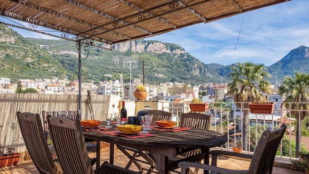 A terrace with a table set for dining, overlooking a coastal town and mountains. -  De Vivo Realty - La Mela Apartment (Meta)