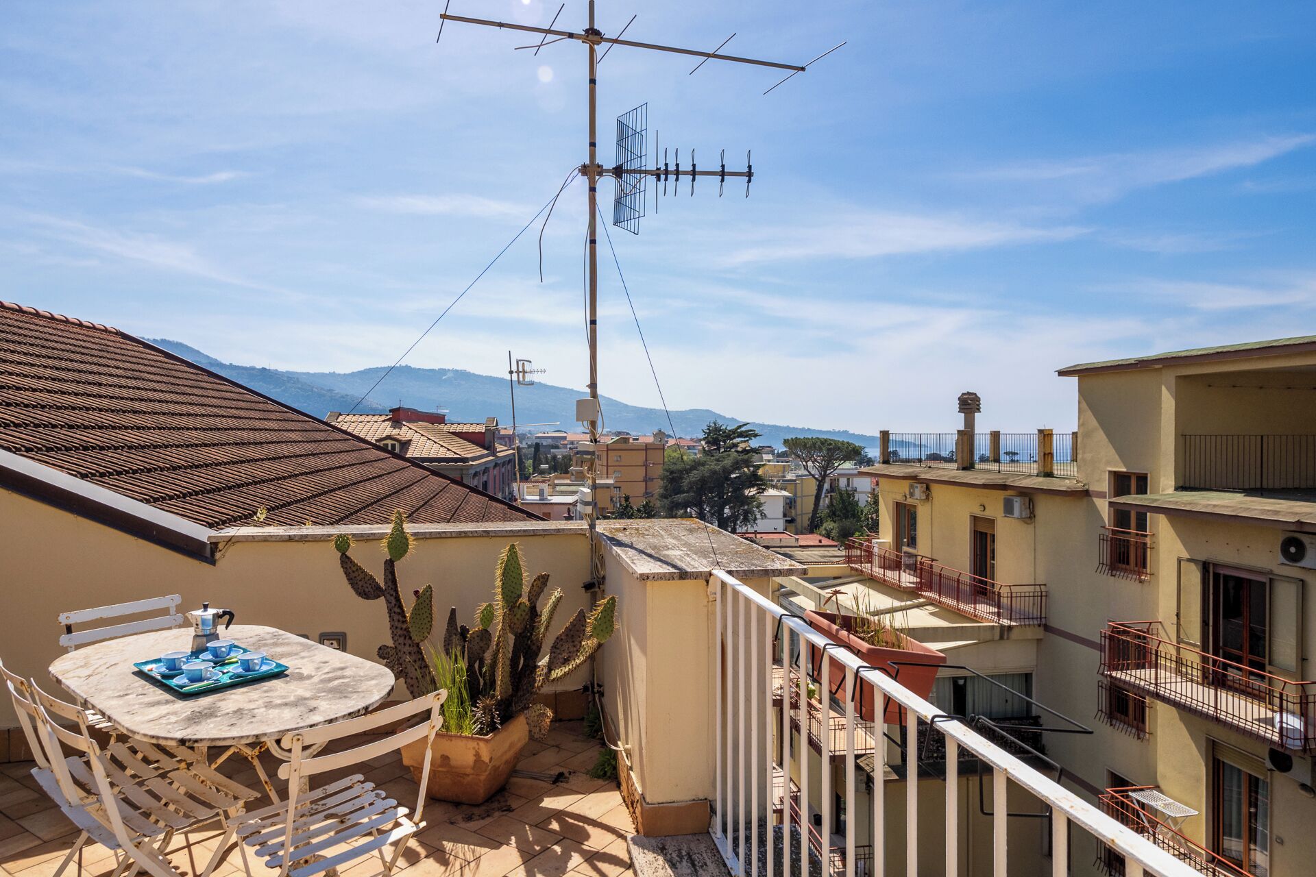 Terraza en la azotea con una mesa lista para comer, una planta de cactus en maceta y una antena grande.