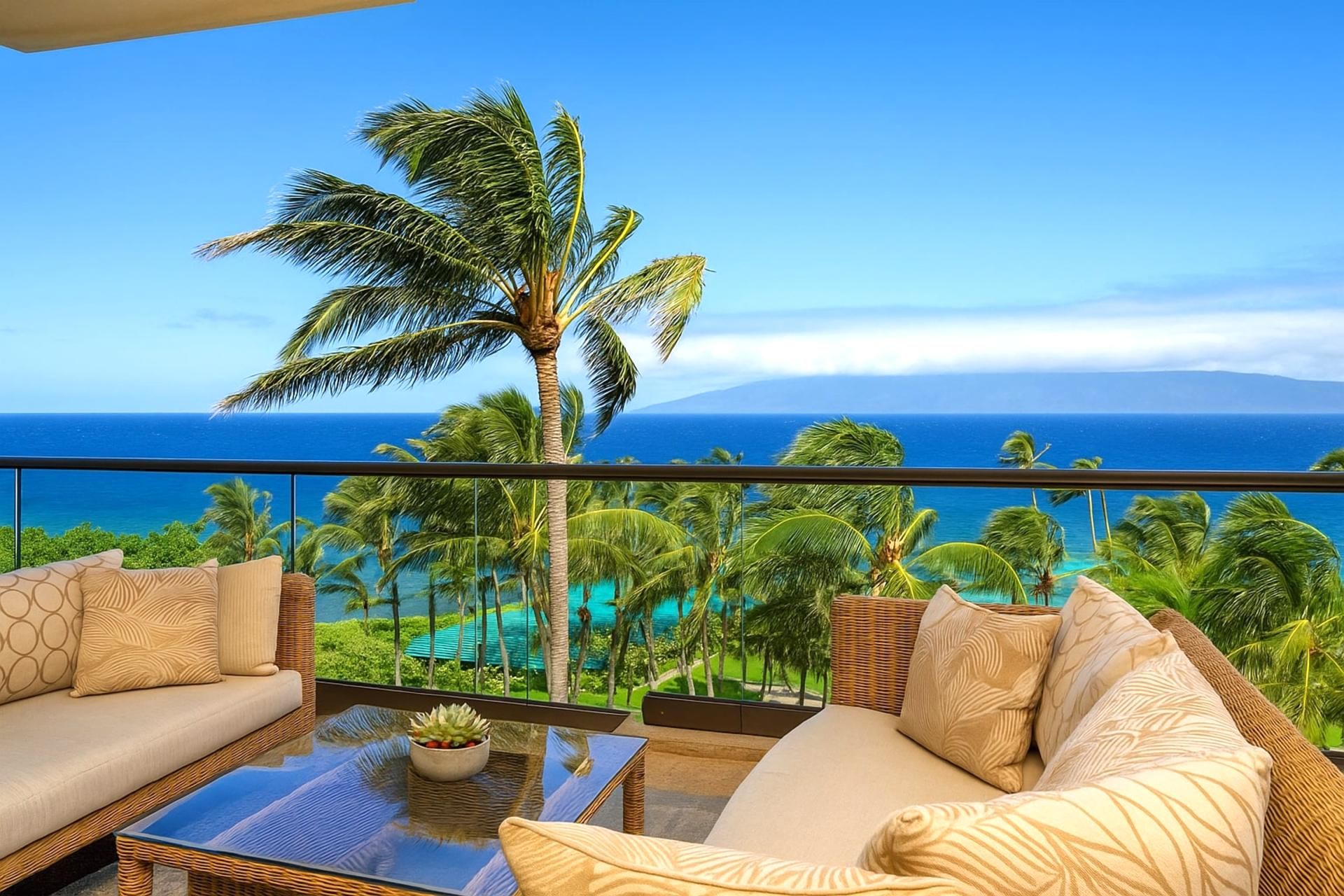 Un balcón con sofá y mesa, con vista a un paisaje tropical de palmeras y al océano.