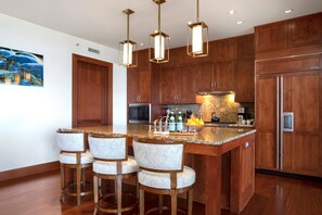 Eine moderne Küche mit Holzausstattung, einer zentralen Kochinsel mit Barhocker, Pendelleuchten und einem Edelstahlkühlschrank.