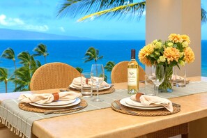 Ein Tisch für zwei Personen, gedeckt mit Wein, Gläsern und einem Blumenstrauß, mit Blick auf einen tropischen Strand.