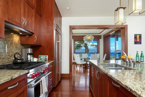 A kitchen with wooden cabinets, granite countertops, stainless steel appliances, and a view to the outside.