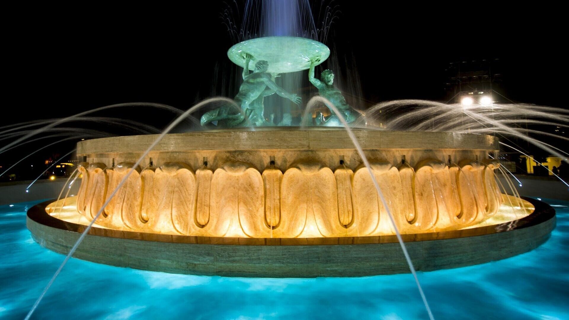 Una fuente nocturna con una escultura central y chorros de agua.