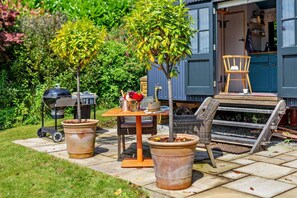 Une terrasse extérieure avec un barbecue, des plantes en pot, une table avec des chaises et un fauteuil en osier.