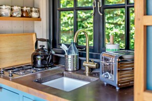 A kitchen with a gas stove, a kettle, a coffee maker, a toaster, and a window with a view of greenery. - 1 Bed in Withypool (oc-s29887) (Withypool)