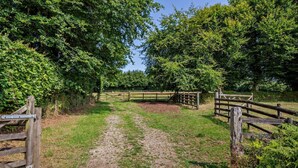 Un sendero rural que conduce a una zona vallada, con camino de tierra y cercas de madera.