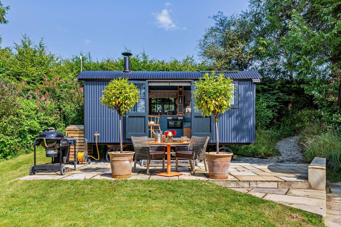 A compact outdoor kitchen area with a barbecue grill, a dining table with chairs, and potted plants.