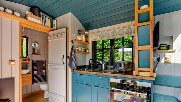 Cocina compacta con horno integrado, lavamanos y ventana con vistas al follaje.