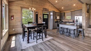 A wooden cabin interior with a dining area, kitchen, and bar stools.