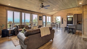 A spacious living area with a large brown leather sofa, wooden flooring, and a ceiling fan.