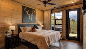 A bedroom with a bed, a nightstand, a ceiling fan, and a window with curtains.