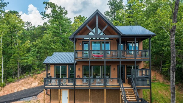 A multi-story cabin with a balcony, large windows, and a metal staircase.