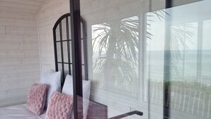 Een slaapkamer met een bed, kussens, een nachtkastje en uitzicht op palmbomen door een glazen deur.